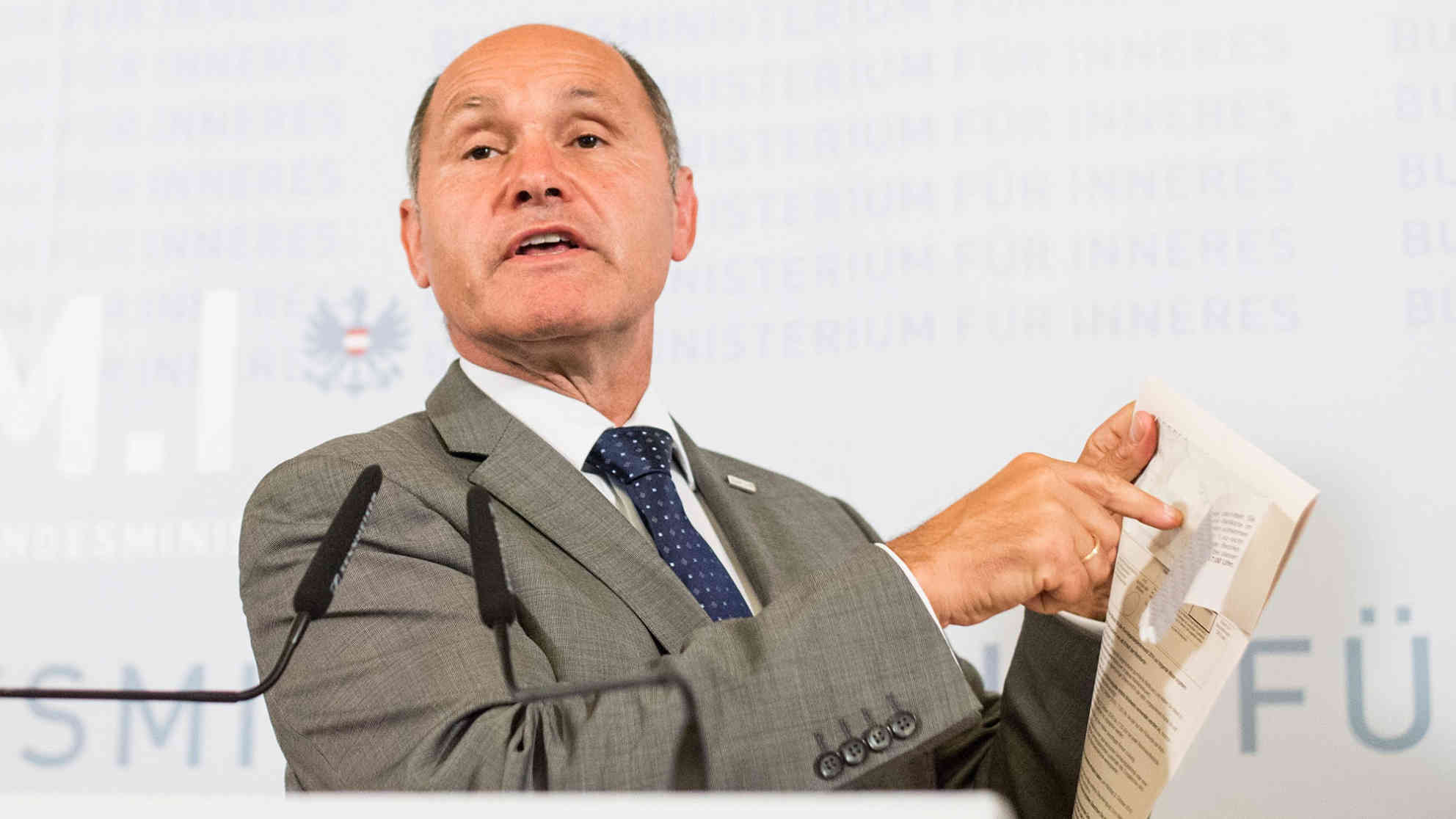 Der österreichische Innenminister Wolfgang Sobotka deutet in der heutigen Pressekonferenz auf den Grund für die Wahlverschiebung: die teilweise defekten Kuverts für die Wahlkarten. Foto: picture alliance | dpa