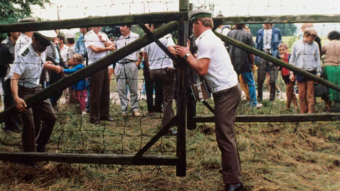 Österreichische Grenzbeamte öffnen ein Grenztor. Etwa 600 DDR-Bürger nutzten ein paneuropäisches Picknick an der ungarisch-österreichischen Grenze, bei dem ein Grenztor symbolisch geöffnet wurde, zur Flucht in den Westen. Aufgenommen am 19. August 1989. Foto: picture-alliance | dpa