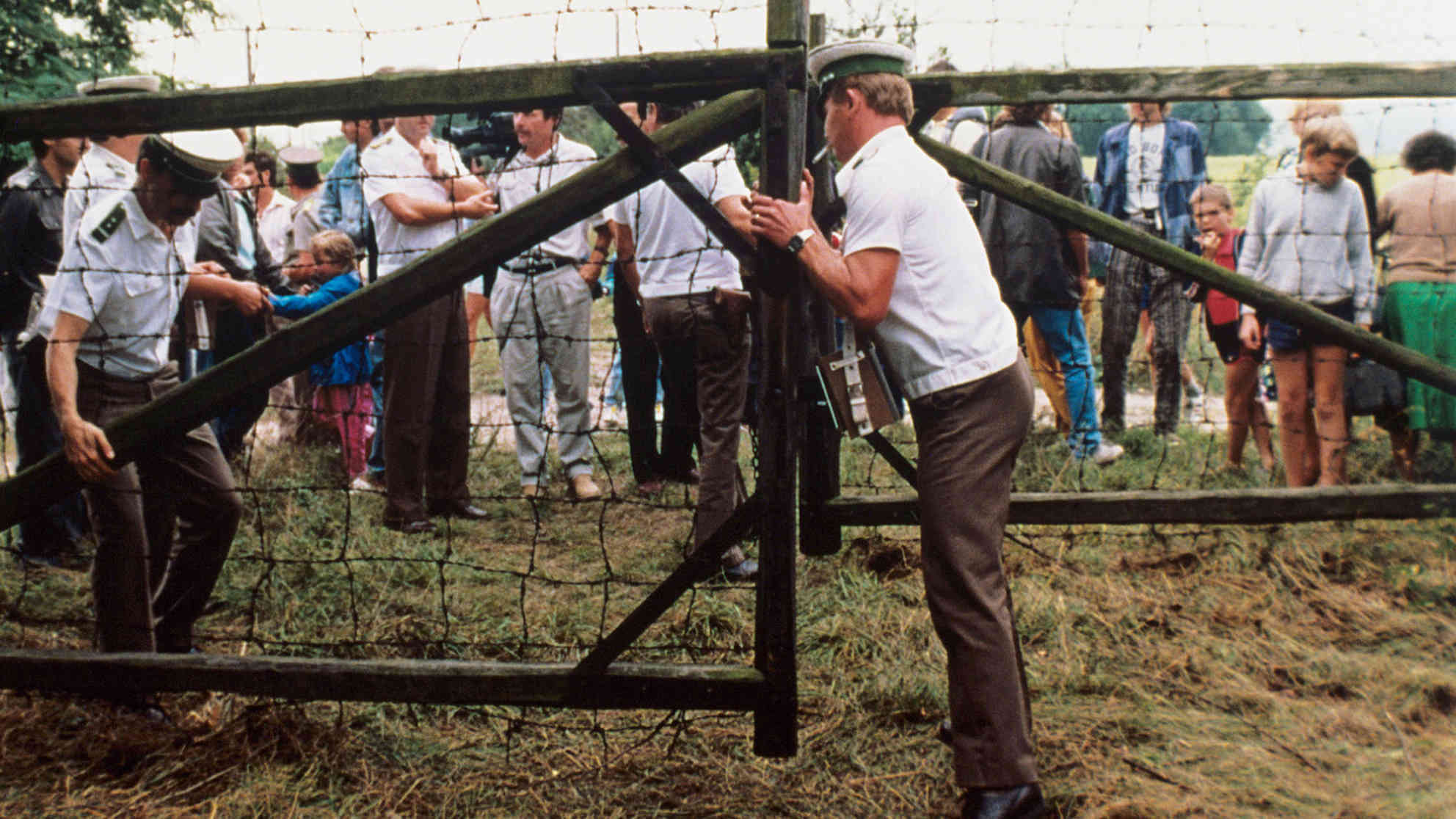 Österreichische Grenzbeamte öffnen ein Grenztor. Etwa 600 DDR-Bürger nutzten ein paneuropäisches Picknick an der ungarisch-österreichischen Grenze, bei dem ein Grenztor symbolisch geöffnet wurde, zur Flucht in den Westen. Aufgenommen am 19. August 1989. Foto: picture-alliance | dpa